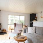 Living room with sofa, armchair, and wood stove. Wooden floor and large windows.