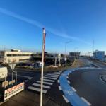 Ansicht von einer Straße mit Radweg und Flagge. Im Hintergrund sind Gebäude und ein Hafen zu sehen.