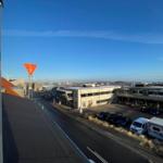 Ausblick auf Straße mit Parkplätzen und Industriegebäude unter blauem Himmel.