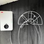 Elektrischer Ladepunkt mit Steckerhalter an schwarzer Holzwand.