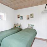 Two beds with green bedding and colorful pillows. White walls and wooden ceiling.