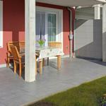 Terrasse mit Tisch, Stühlen und Sonnenschutz. Neben einem Gartenhaus mit Tür und Fenster.