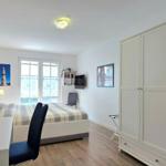 Schlafzimmer mit Bett, Schreibtisch, Kleiderschrank und Fenster.