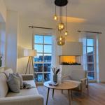 Wohnzimmer mit Sofa, Sessel, Tisch und Kamin. Fenster mit Blick auf Terrasse.