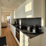 Moderne Küche mit weißen Schränken und dunkler Arbeitsplatte. Blick in das Wohnzimmer.