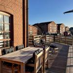 Terrasse mit Holztisch und Stühlen, Blick auf Gebäude und Krane.
