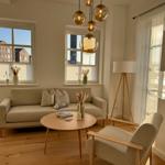 Wohnzimmer mit Sofa, Sessel und runden Tisch. Fenster und Hängelampen.