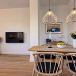 Esszimmer mit Holztisch, Stühlen und zwei Hängelampen. Fernseher an der Wand.