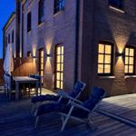 Terrasse mit Liegestühlen und Tisch vor Backsteinhaus bei Dämmerung.