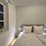 Schlafzimmer mit Bett, zwei Nachttischen und Fenster mit Pflanzen.