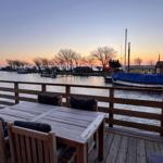 Terrasse mit Tisch und Stühlen über Wasserblick zum Sonnenuntergang.