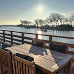 Holztisch mit Stühlen auf Terrasse mit Blick auf Wasser und Boote.