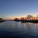 Sonnenuntergang über Hafen mit Booten und Bäumen am Ufer