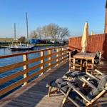 Holzterrasse mit Liegestühlen und Tisch am Wasser mit Boot.