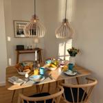 Esszimmer mit Holztisch, Stühlen und hängenden Lampen. Tisch gedeckt mit Frühstück.