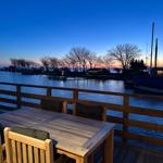 Terrasse mit Tisch und Stühlen an Wasserfront bei Sonnenuntergang.