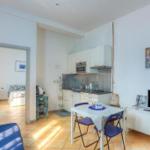 Living kitchen with dining area, bedroom in background, and TV furniture.