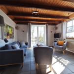 Wohnzimmer mit Sofa, Sessel und TV. Holzdecke und große Fenster.