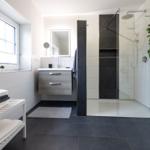 Badezimmer mit Dusche, Waschbecken und Fenster. Handtuchständer und Pflanzen sind sichtbar.