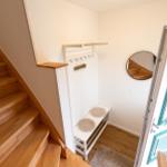 Eingangsbereich mit Holztreppe, Kleiderständer und runder Wandspiegel.