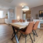 Esszimmer mit Holztisch und braunen Stühlen. Küche und Wohnbereich im Hintergrund.