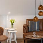 Ein Wohnbereich mit braunem Sofa, weißen Tischen und hängenden Lampen.