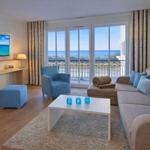 Wohnzimmer mit Sofa, Sessel und Balkonblick aufs Meer.