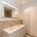 Flur mit Garderobe und Blick in Schlafzimmer mit Holzboden und Wandbild.