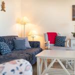 Wohnzimmer mit Sofa, Sessel und Tisch. Wandbilder zeigen Leuchtturm und Strand.