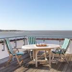 Terrasse mit Tisch und Stühlen, Blick auf Wasser und Horizont.