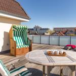 Dachterrasse mit Strandkorb, Tisch und Liegestühlen. Blick auf Stadt und Dächer.