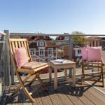 Terrasse mit zwei Holzstühlen, Tisch und roten Kissen. Blick auf Wohnhäuser und Straße.