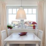 Esszimmer mit weißem Tisch, Stühlen und Fensterblick auf Dächer.