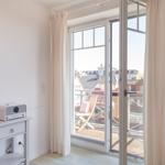 Zimmer mit Balkon, Blick auf Dächer, weiße Wände, Schrank und Radio.