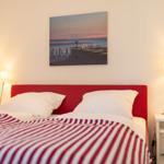 Schlafzimmer mit rotem Kopfteil, gestreifter Bettdecke und Wandbild über dem Bett.