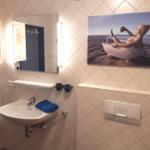 Badezimmer mit Waschbecken, Spiegel und Wandbild.