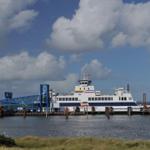 Fährschiff am Hafen mit blauem Steg und bewölktem Himmel.