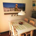 Esszimmer mit Tisch, Stühlen und Wandbild. Mikrowelle und Küchenzeile sichtbar.