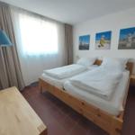 Schlafzimmer mit Doppelbett, Holzmöbel und Fenster mit Vorhängen.