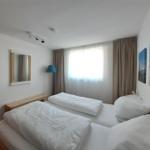 Zimmer mit Doppelbett, Fenster, Vorhängen und Wandbildern.