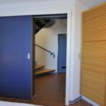 Schlafzimmer mit Schiebetür und Holzschrank. Treppenhaus im Hintergrund.