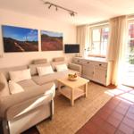 Wohnzimmer mit Sofa, Couchtisch und TV. Fenster und Glastür führen auf eine Terrasse.