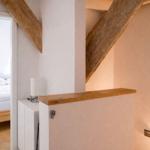 Schlafzimmer mit Holzbett und Dachschräge. Holzgeländer und Wandbeleuchtung sichtbar.