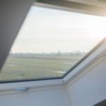 Dachfenster mit Blick auf grünes Feld und Windräder im Hintergrund.