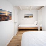 Schlafzimmer mit Bett, Wandbild und Holzboden. Durchgang zu einem weiteren Raum.