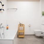 Badezimmer mit Badewanne, Toilette und Waschbecken. Dekorative Elemente wie Rettungsring und Segelboot.