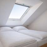 Schlafzimmer mit Dachschrägen und Dachfenster. Bett mit weißer Bettwäsche.