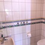 Badezimmer mit Fliesen, Waschbecken, Toilette und Toilettenpapierhalter.