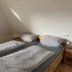 Zimmer mit zwei Einzelbetten, Holzgestell und Nachttischen mit Lampen.