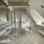 Badezimmer mit Dusche, Toilette und Waschbecken unter Dachschrägen.